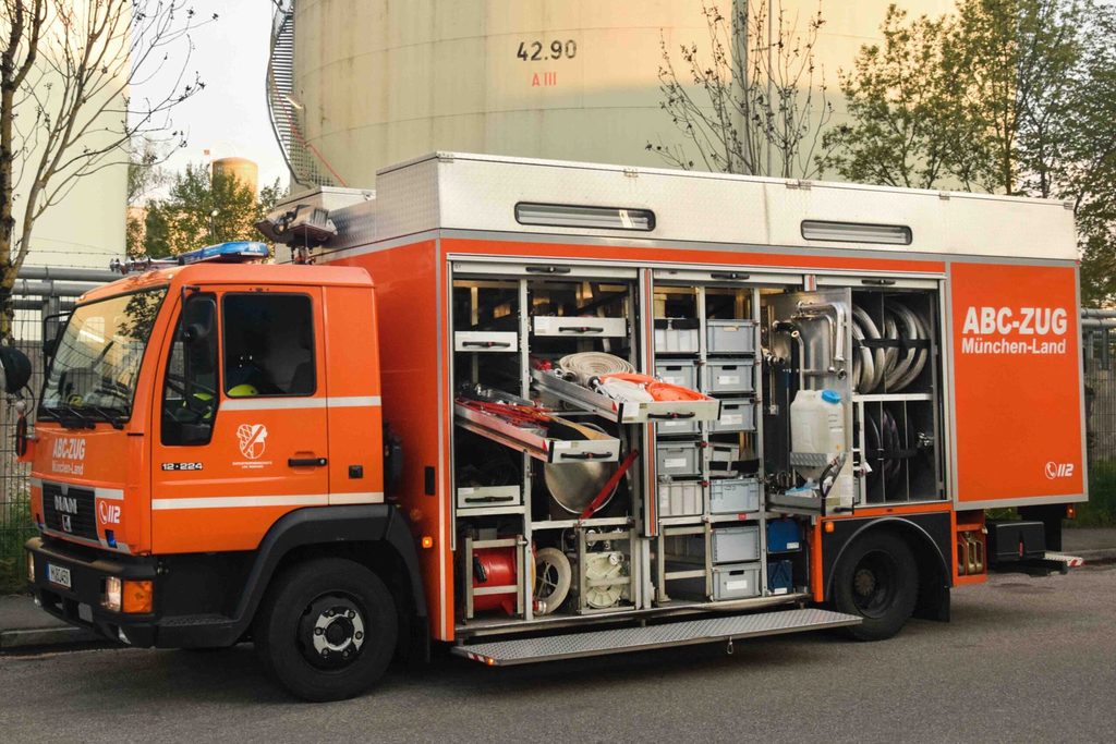 Bild des Gerätewagen Gefahrgut. Ein organe-grauer Lkw vor einer Tanklager.